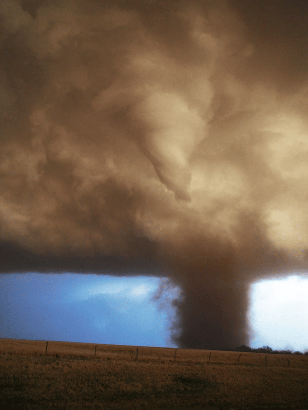 A mature tornado has formed from the ground up. It has a distinct funnel in the clouds and a wide dark spout from the ground into the clouds. 