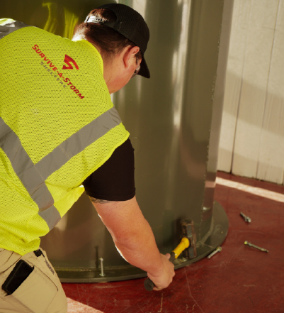 residential tornado shelter installation Technician anchoring a residential tornado shelter to the floor during installation.