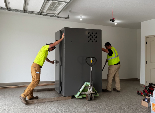 Professional installers positioning an above-ground tornado shelter inside a residential garage